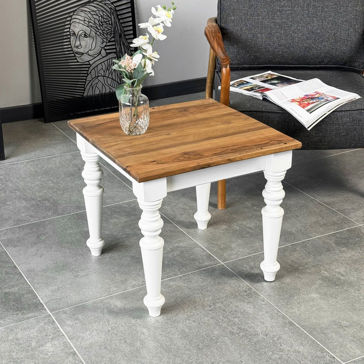Square walnut side table with white turned legs in a living room beside a gray armchair