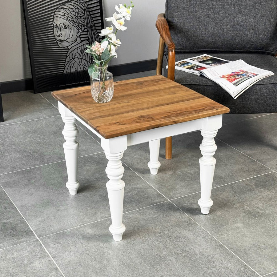 Square walnut side table with white turned legs in a living room beside a gray armchair