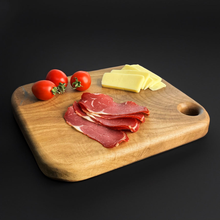 Walnut wood cutting board with rounded corners and a hanging hole, angled view with sliced meat on top