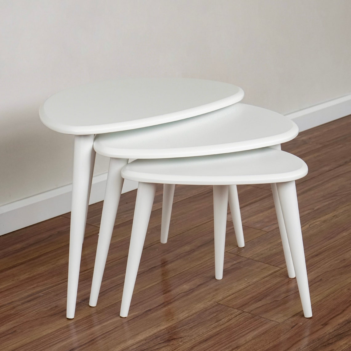 White gloss nesting coffee tables with tapered legs seen from the left with the tops empty