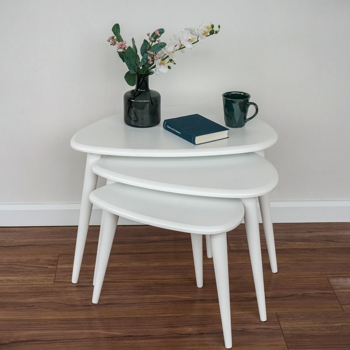 Set of 3 white gloss lacquer nesting coffee tables in front of a white wall, seen from the front