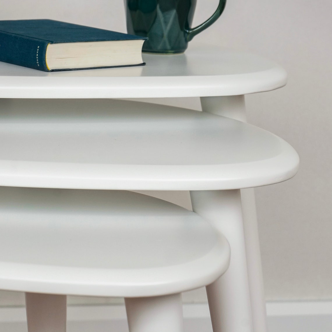 Close-up of the rounded edges of the three white high gloss nesting table tops, with a mug on top