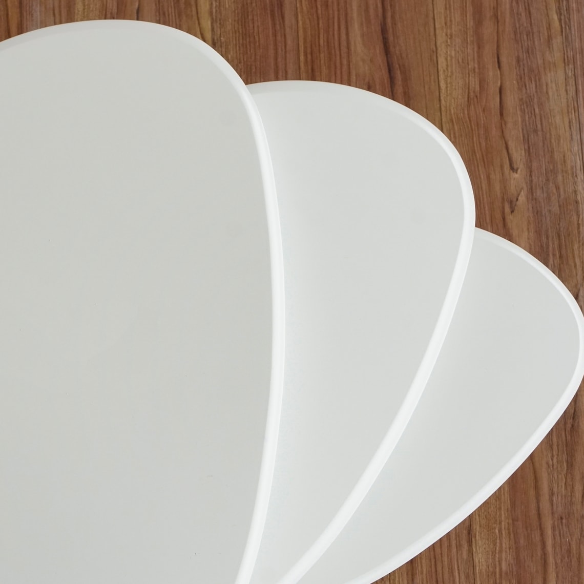 Top-down view of three white high gloss lacquer nesting table tops fanned out on a wood floor