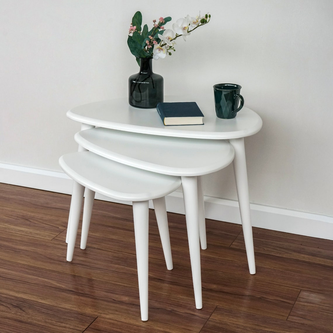 White nesting coffee tables with tapered legs, smallest table pulled forward, from the left with a book on top