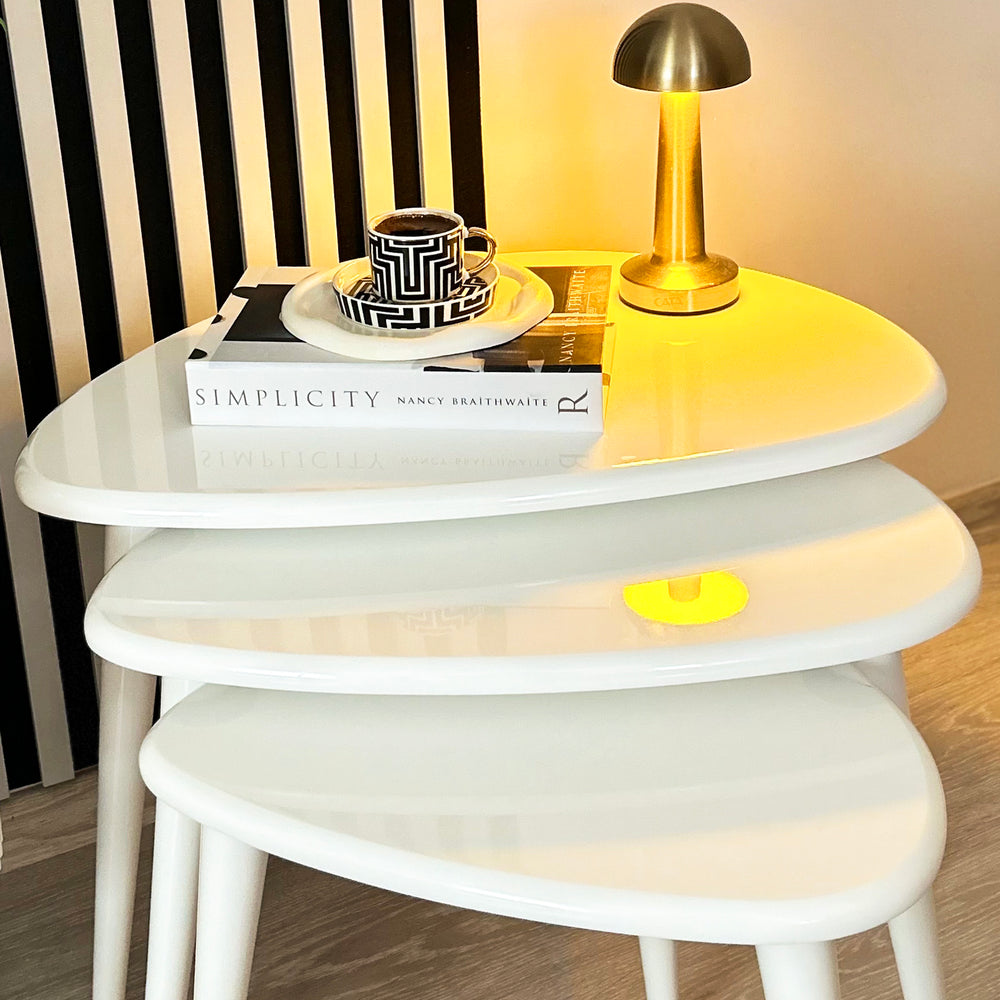 Set of white nesting tables with a gold lamp and decorative items on top.