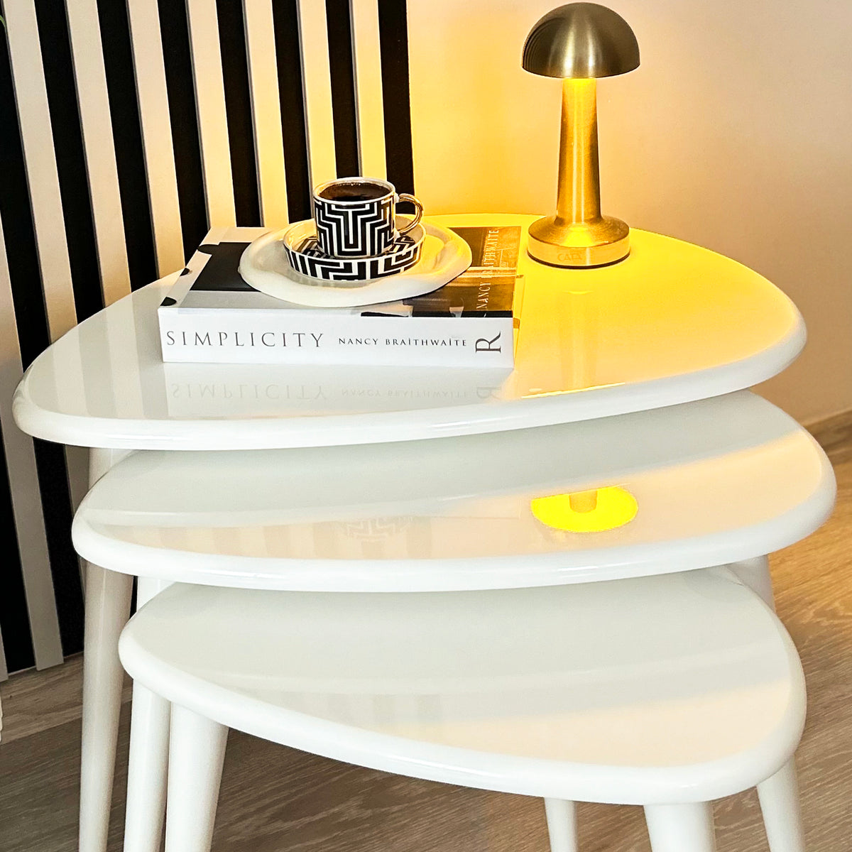 Close-up of three white high gloss lacquer nesting tables with tapered legs and a gold lamp on top