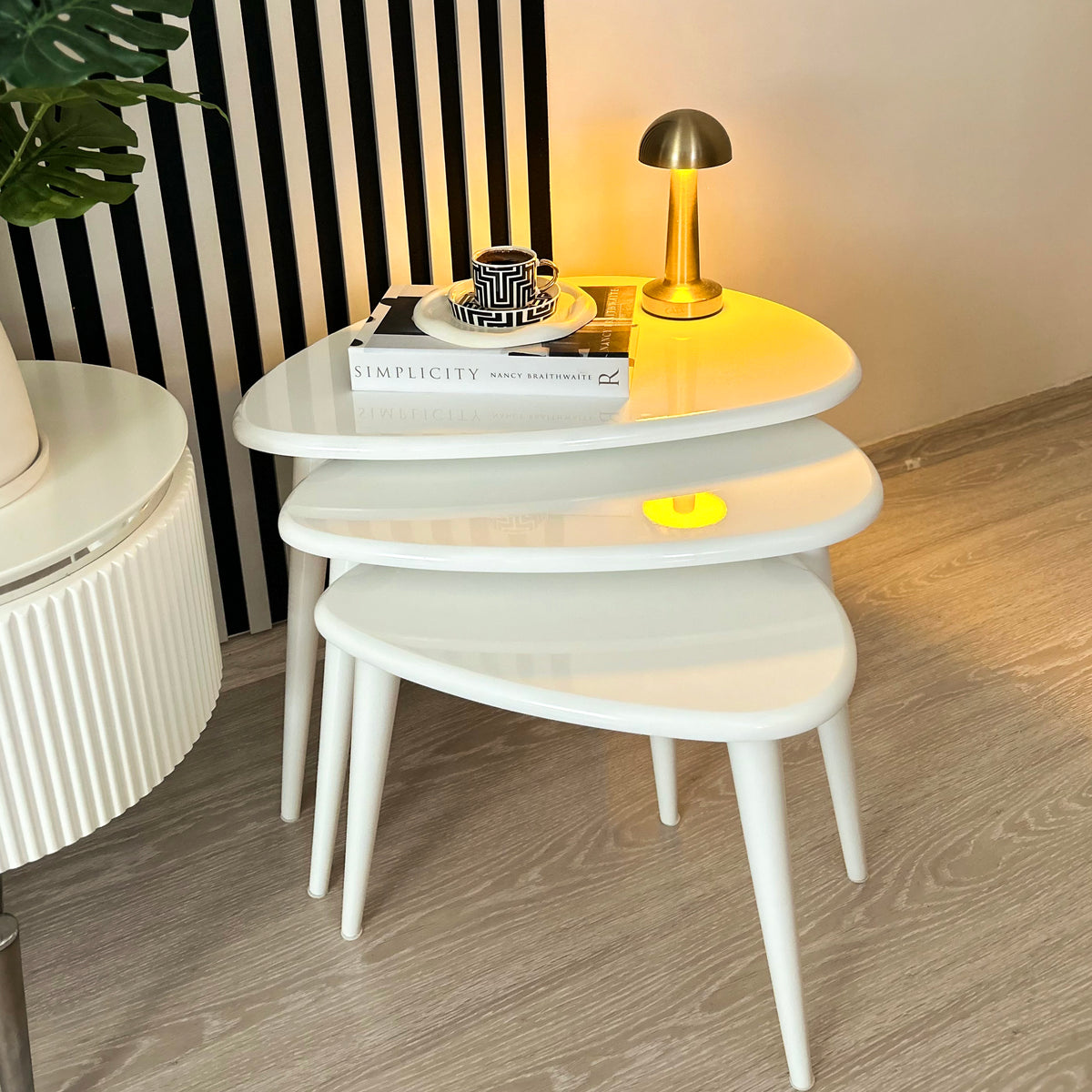 Three white gloss lacquer nesting tables with tapered legs, from the front with a cup on the top table