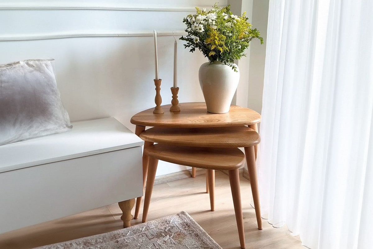 Set of three wooden nesting tables with flowers and candles beside a white sofa