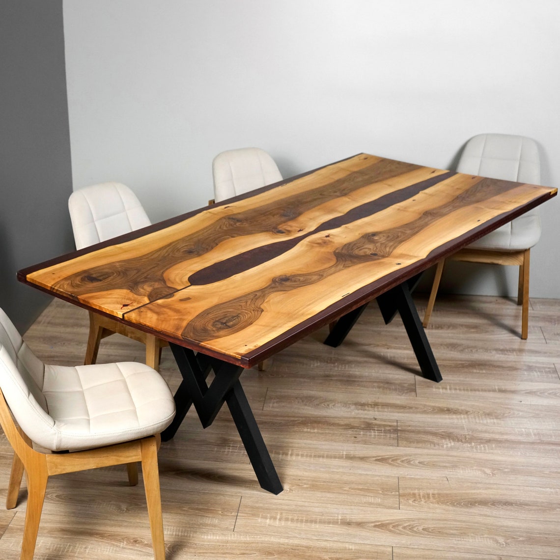 Walnut dining table with burgundy epoxy river and black X-shaped metal legs, three-quarter view with chairs