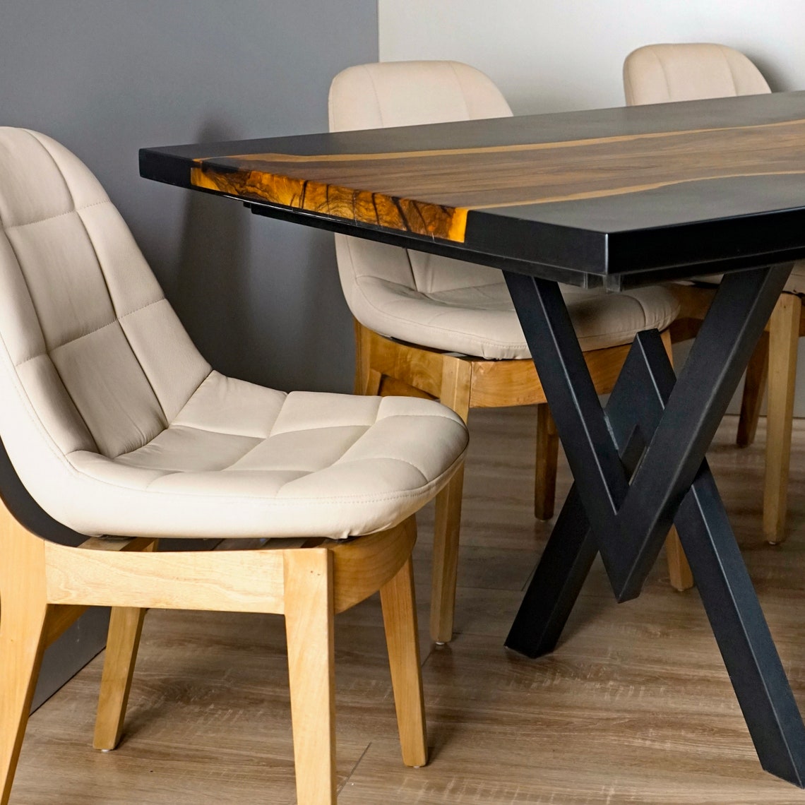 Close-up of the walnut live edge strip, black epoxy edge and X shaped leg beside a cream chair