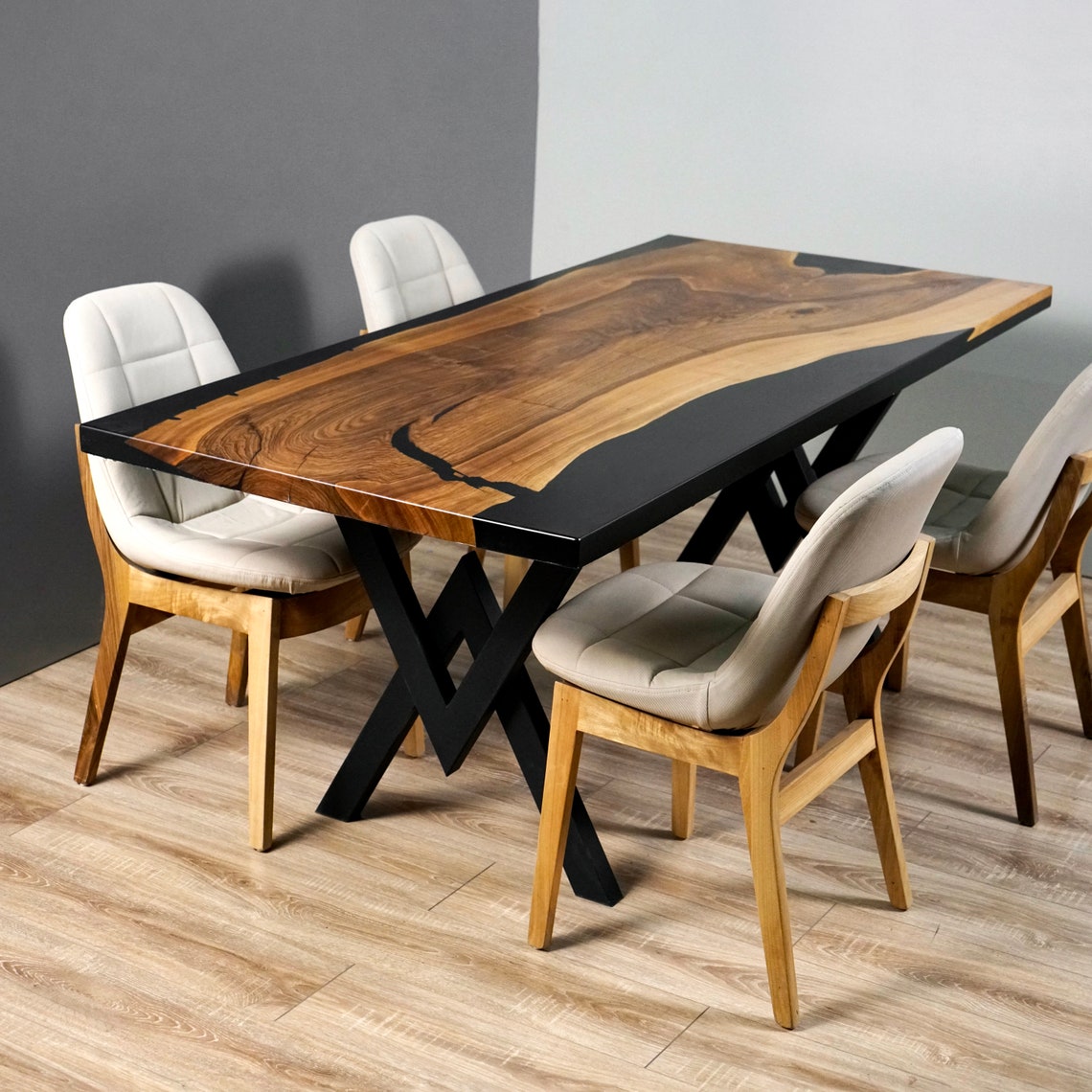 Live edge walnut dining table with black epoxy river and X-shaped metal legs, three-quarter view with four chairs