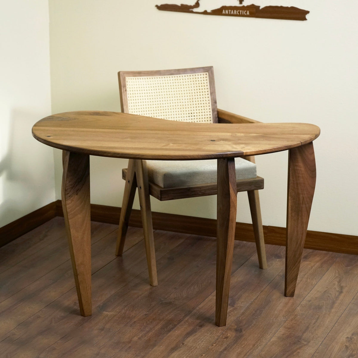 Walnut desk seen from the room corner with the kidney shaped top and a chair pulled underneath