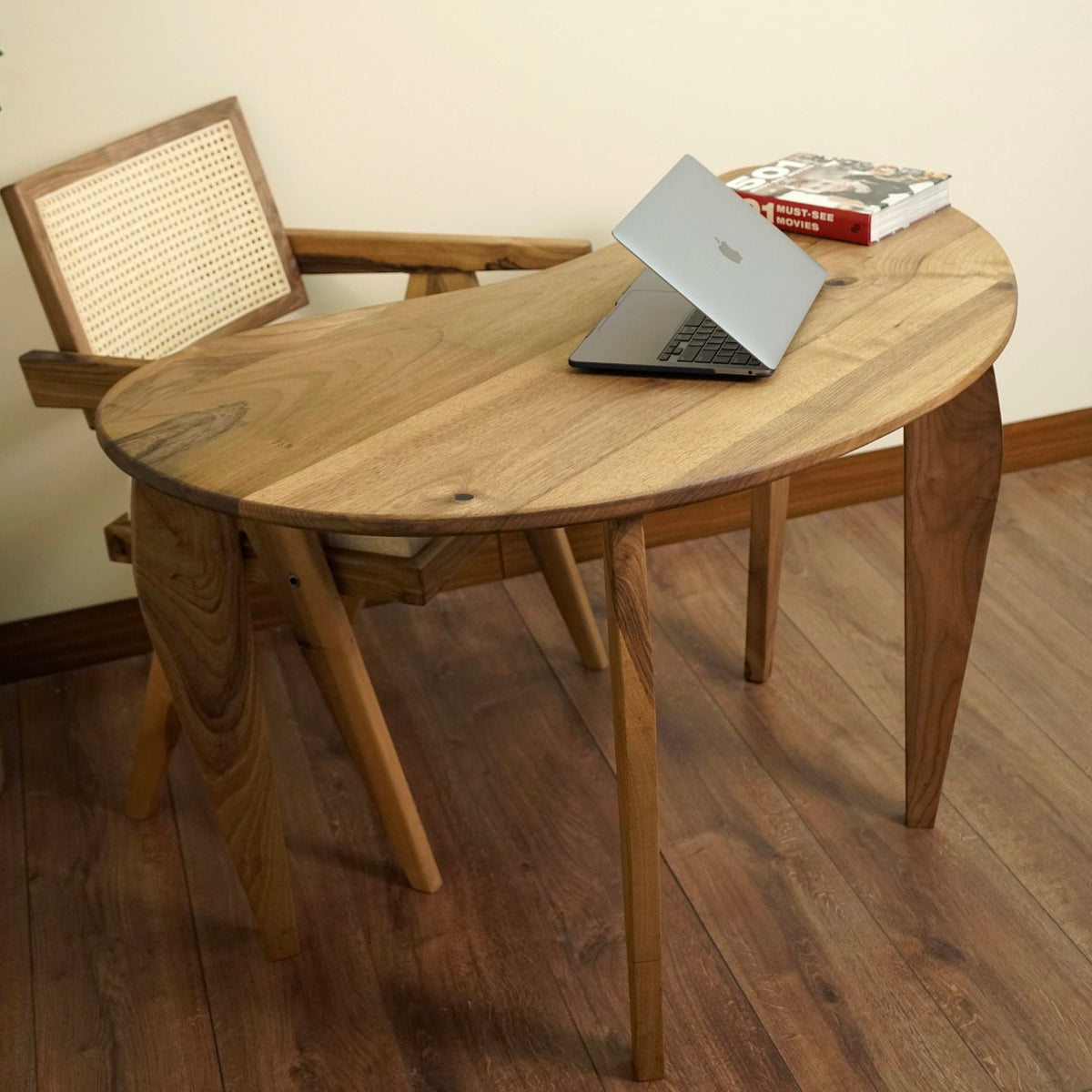 High angle of the walnut desk's curved top with a laptop, from beside the rattan chair