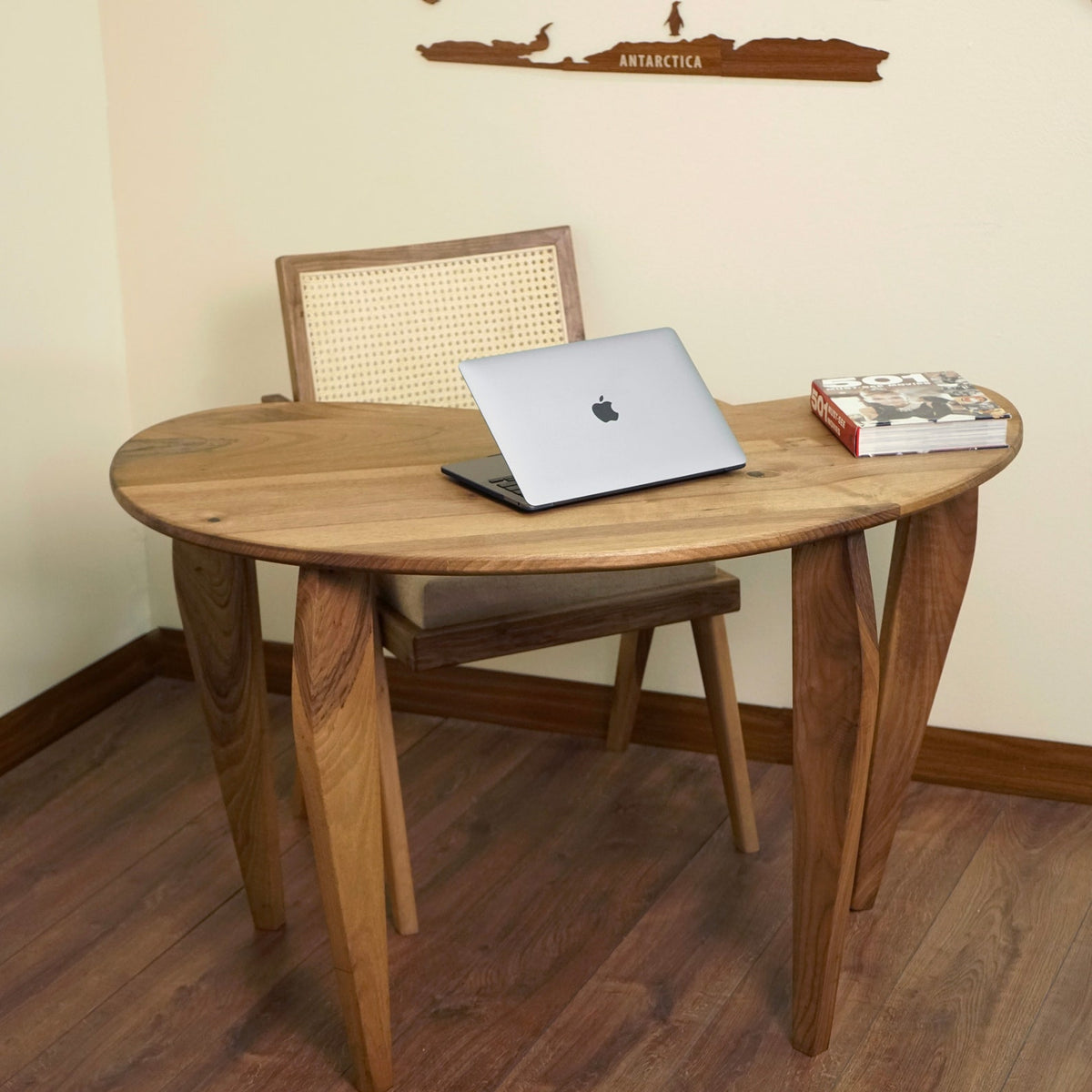 Front view of the bean shaped walnut desk with a laptop and a rattan back chair tucked in