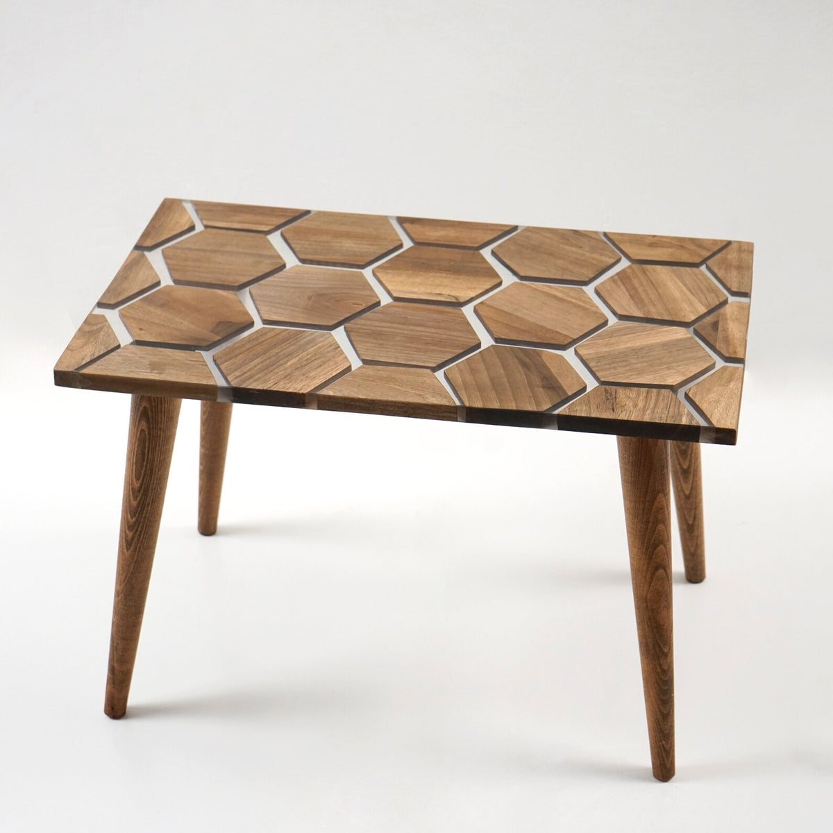Honeycomb walnut epoxy coffee table from a low angle with its four tapered wooden legs on gray