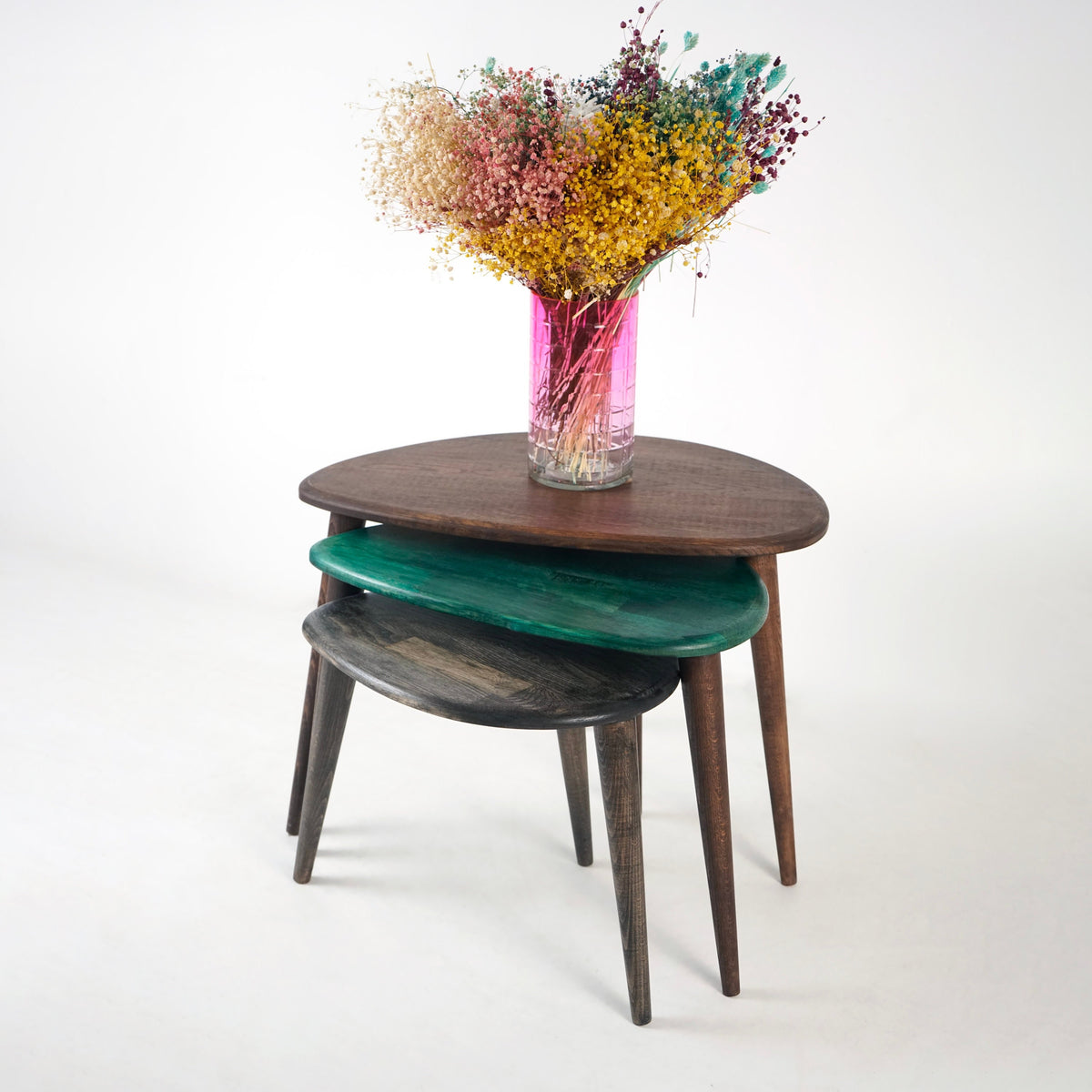 Multicolor oak nest of three pebble tables with a vase of dried flowers on a plain background