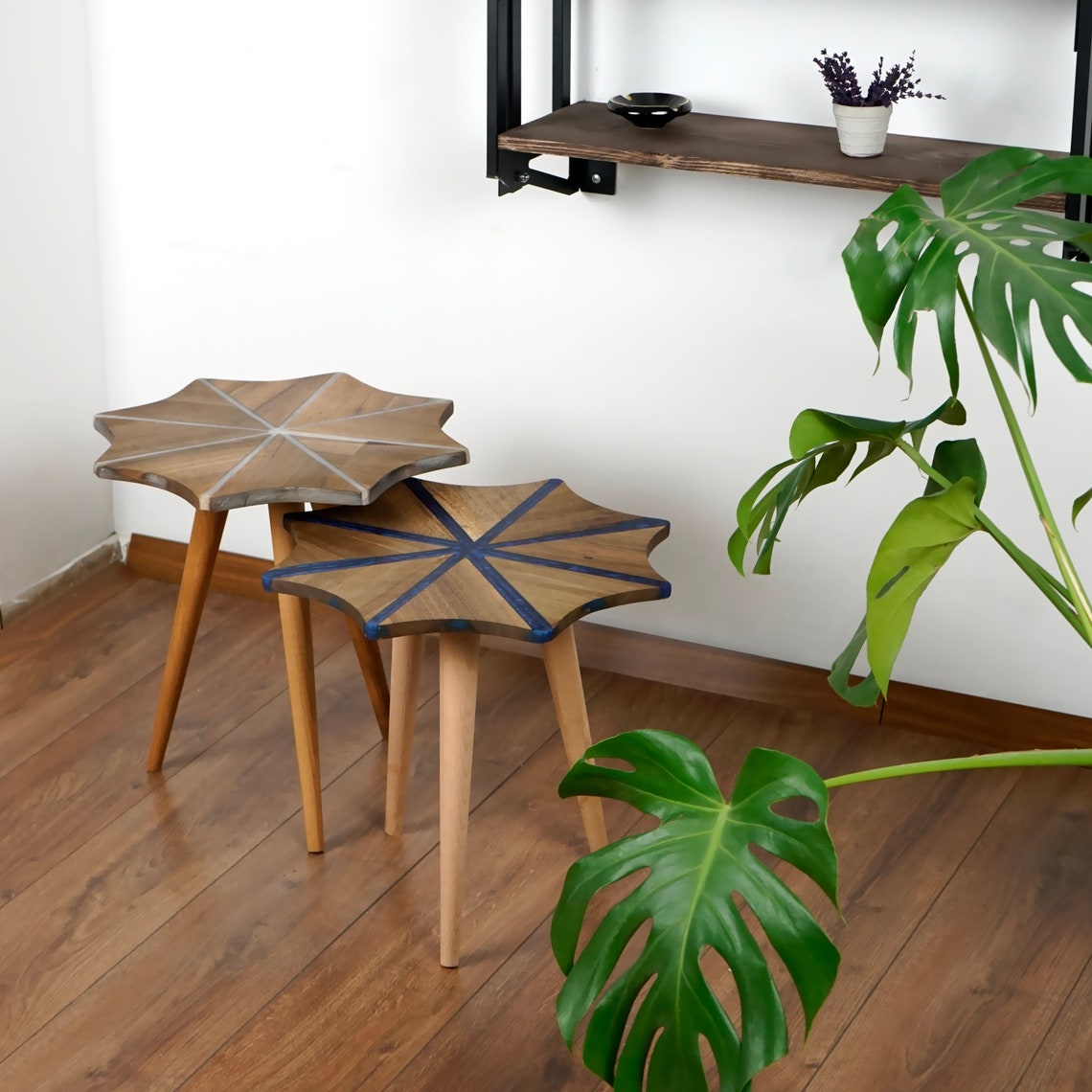 Two nested walnut snowflake side tables with tripod wooden legs beside a monstera plant