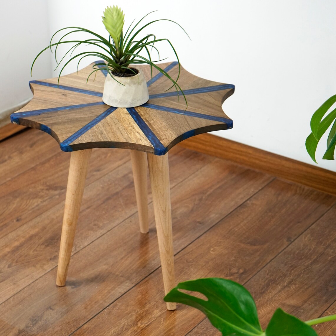 Walnut snowflake side table with blue epoxy stripes and natural wood tripod legs, with an air plant on top